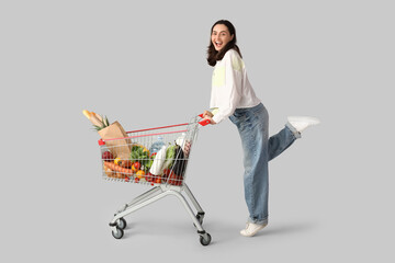 Beautiful young happy woman with full shopping cart on grey background © Pixel-Shot