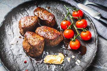 Filet mignon steaks with cherry tomatoes on a black mica plate, With gray napkin and cutlery. Top...