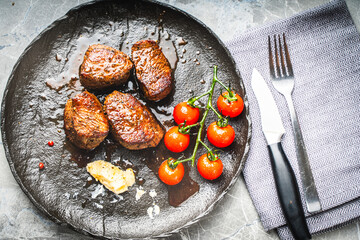 Filet mignon steaks with cherry tomatoes on a black mica plate, With gray napkin and cutlery. Top view
