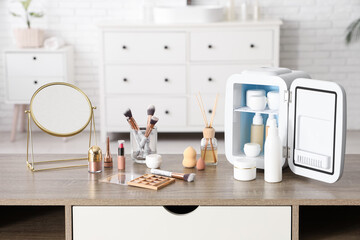 Small cosmetic refrigerator, diffuser and mirror on table near white wall. Closeup