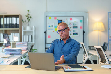 Senior manager gesturing while video conferencing on laptop in modern office, demonstrating leadership and communication in corporate setting