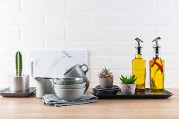 Kitchen Ceramic Cookware Set On Wooden Countertop, Oil In Bottles For Cooking. Plants. Front view. White brick wall. Modern style of kitchen space