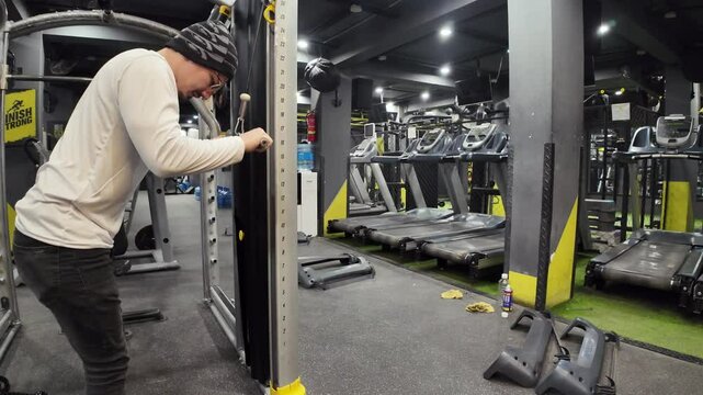 Young Man Doing Triceps Pushdowns in an Empty Gym, with Treadmills, Maintenance Equipment, and Cinematic Lighting in the Background, Captured in Slow Motion