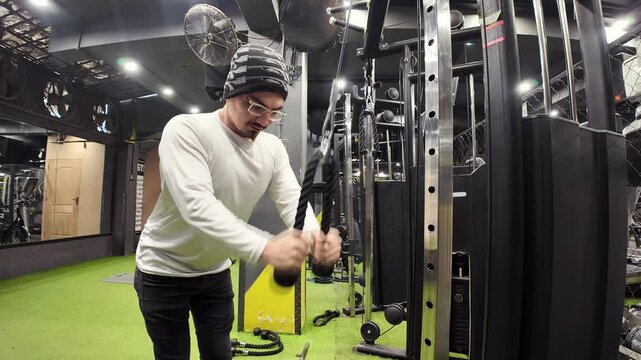 Young Man Doing Triceps Pushdowns with a Rope in an Empty Gym, with a Large Mirror and Gym Equipment in the Background