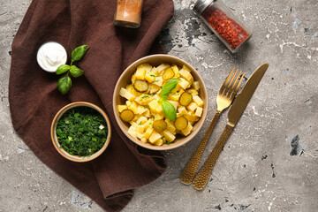 Bowl of tasty potato salad with pickled cucumber and basil on grey background