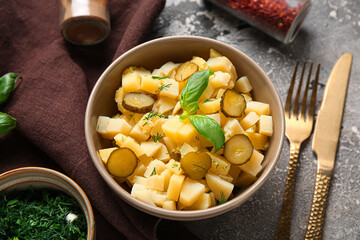 Bowl of tasty potato salad with pickled cucumber and basil on grey background