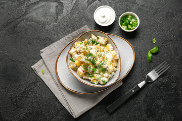 Bowl of tasty potato salad with sauce and dill on black background