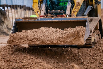 Track compact loader working in construction project leveling the ground and excavating materials...