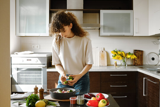 Woman adding fresh zucchini to a pan with vegetables for baking