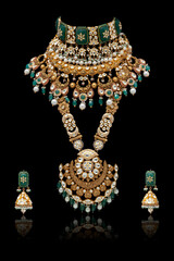 A stunning heavy gold necklace and earrings featuring green emeralds, rubies, and diamonds, against a black background.