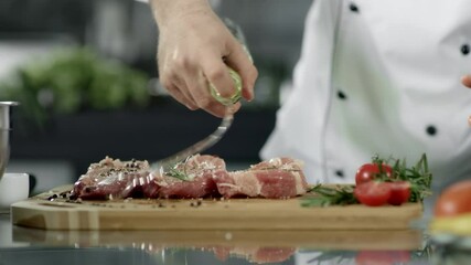 Chef prepares raw steak with herbs and spices in kitchen for restaurant
