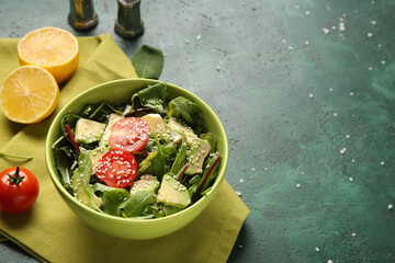 Bowl of tasty avocado salad with cherry tomatoes and lemon on green background