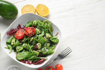 Bowl of tasty avocado salad with cherry tomatoes and lemon on white wooden background