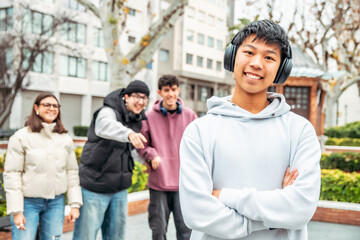 Happy multiracial group of students having fun together in a university campus, a chinese teenager with headphones is smiling with crossed arms and his friends are pointing at him
