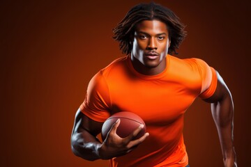 A man in an orange shirt is holding a football