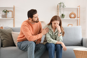 Obraz premium Young man apologizing to his crying wife on sofa at home