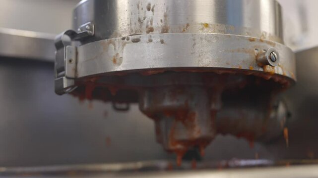 A machine is spitting out red sauce. The sauce is dripping down the side of the machine. The machine is silver and has a lot of rust on it