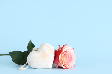 Composition with rose flower and decorative heart on blue background. Valentine's Day celebration.
