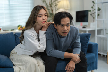 Happy young asian couple relaxing together on a comfortable sofa, enjoying a cozy evening while watching television in their inviting living room, cherishing quality time and connection