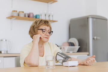 Senior woman with hypertension measuring blood pressure herself at home. Sad Elderly lady measure...