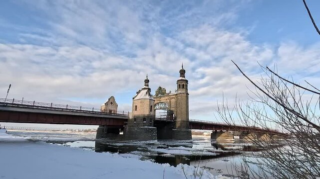 Stone bridge over the river with floating ice floes. Landscape of a winter sunny day.
