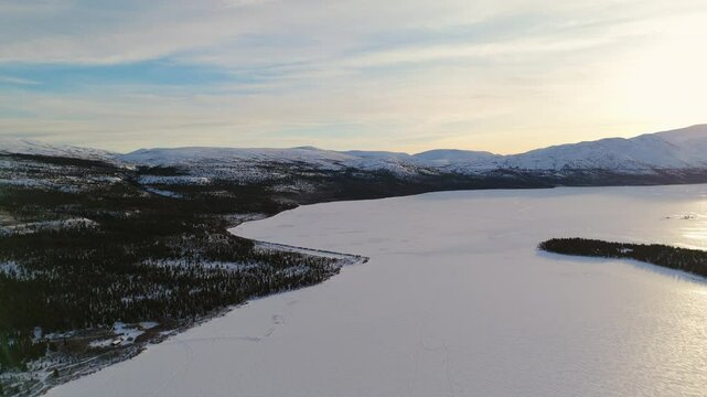 A breathtaking aerial view of Fish Lake, Whitehorse. The pristine Canadian wilderness sparkles under sub-zero skies, surrounded by snowy mountains.
