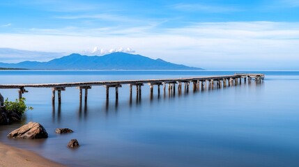 Serene coastal scene with a wooden pier and distant mountains.