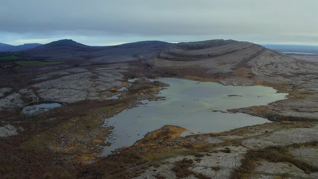 Dynamic aerial pullback showcasing a turlough against the iconic Burren mountains, County Clare.