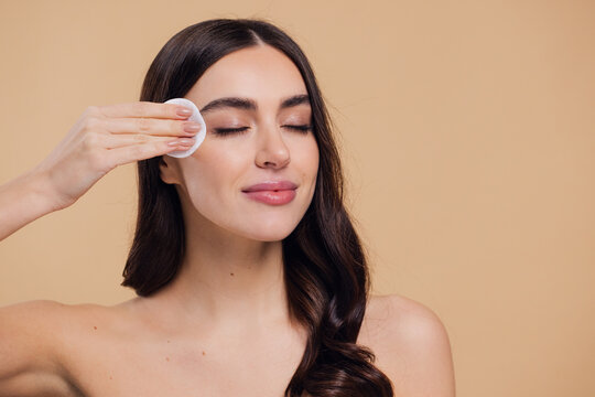 Beautiful brunette half-naked woman removes makeup from the face with a cotton pad