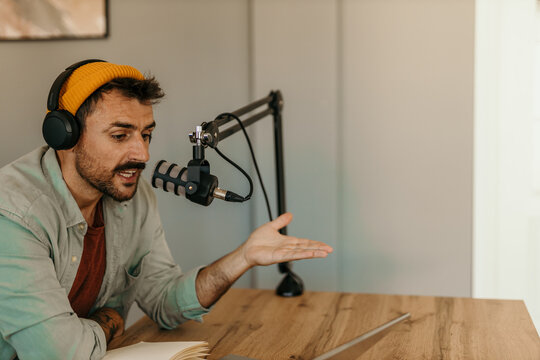 Focused smiling man hosting a podcast with headphones on and a laptop nearby
