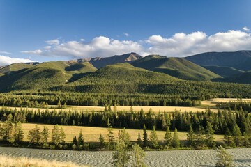 A calm mountain river flows through a picturesque forest landscape surrounded by majestic mountains.