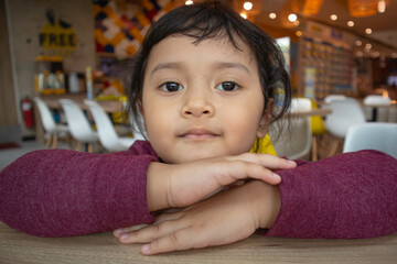 Smiling toddler girl with serious face resting on folded hands