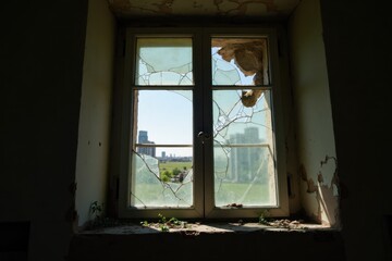 Fototapeta premium A close-up of a broken window in a derelict building, with shards of glass reflecting the light, surrounded by peeling paint and crumbling walls