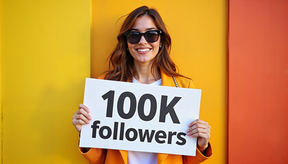 Smiling woman holding "100K followers" sign on vibrant background, social media milestone