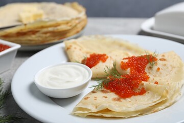 Tasty crepes with red caviar, dill and sauce on grey table, closeup