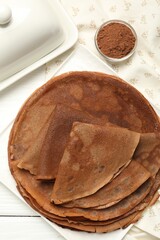 Delicious chocolate crepes and cocoa powder on white wooden table, top view
