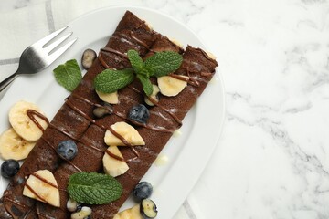Delicious chocolate crepes with banana and blueberries served on white marble table, top view. Space for text