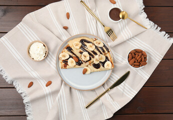 Delicious crepes with chocolate sauce, banana and almonds served on wooden table, flat lay