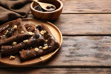 Delicious chocolate crepes with pine cone jam and nuts on wooden table, closeup. Space for text