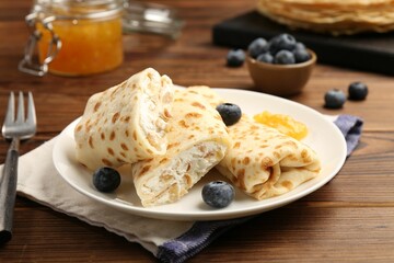 Delicious crepes with cottage cheese, jam and blueberries served on wooden table, closeup