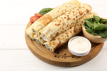 Tasty rolled crepes with cottage cheese and spinach served on white wooden table, closeup