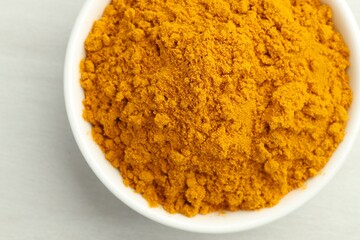 Turmeric powder in bowl on white table, closeup. Top view