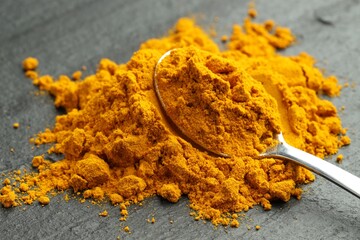 Turmeric powder and spoon on grey table, closeup