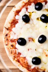 Pizza with mozzarella cheese and black olives on wooden background. Soft focus. Top view. Close up
