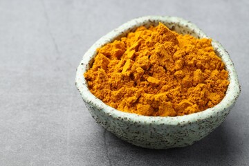 Turmeric powder in bowl on grey table, closeup. Space for text