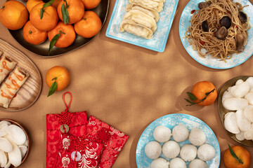 Chinese New Year food arrangement on a table, featuring dumplings, noodles, oranges with red envelopes for gifts