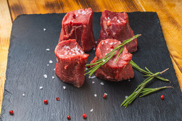 Raw filet mignon steaks with coarse salt and rosemary on a black mica board on a wooden background