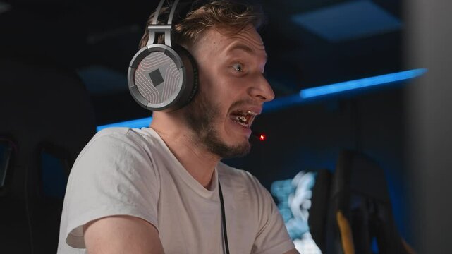 E-sports gamer plays shooter game on PC at cyber space cafe during cybersport tournament. Adult man plays strategy at computer game on desktop. Guy screams while playing video game facial expressions