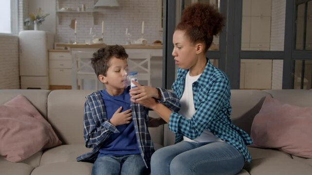 Emotionally stressed African American mother looking for portable asthma inhaler to treat asthma attack of ill cute school age black son in domestic room.