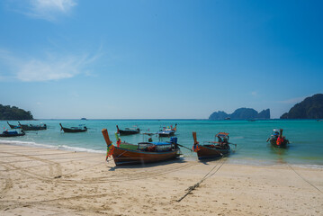 Longtail boats with colorful ribbons rest on a sandy beach in Koh Phi Phi, Thailand, with turquoise...